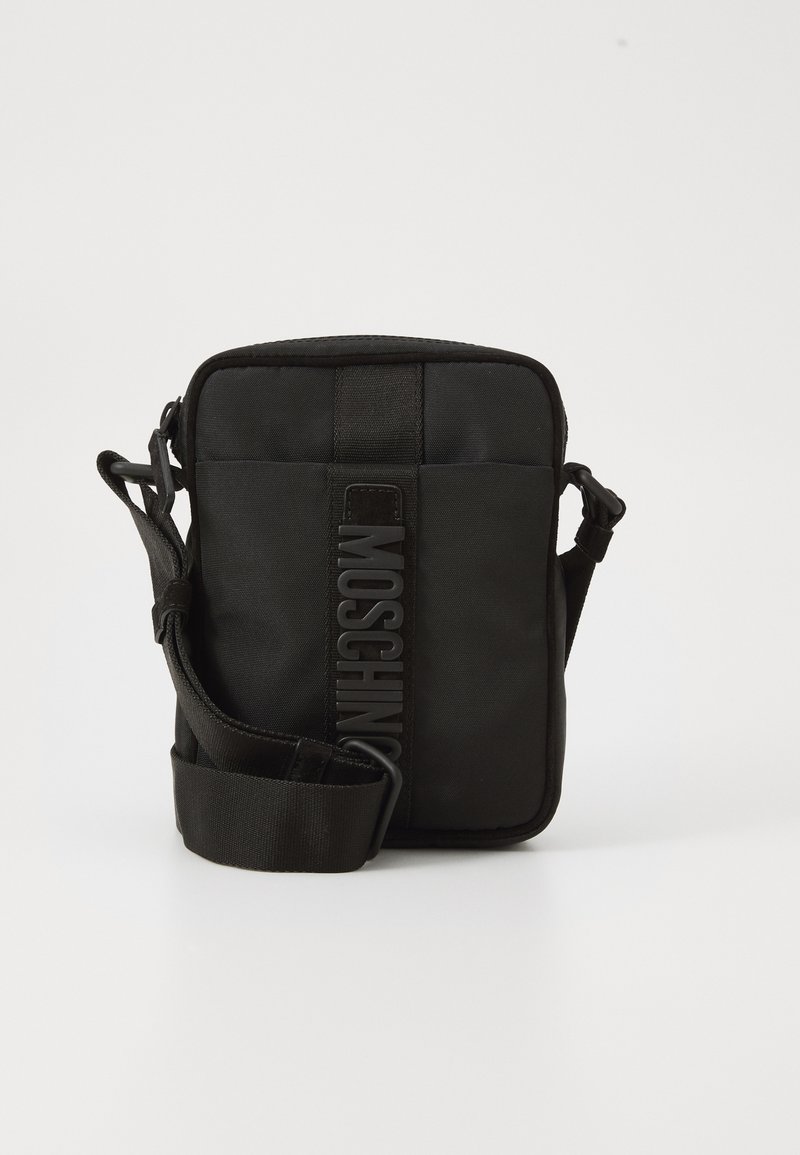 Kompakt svart crossbody-väska med justerbar rem och vertikalt MOSCHINO-logotyp på framsidan mot vit bakgrund.