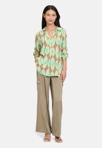 Camicia a maniche lunghe, con colletto, con un motivo geometrico colorato in verde, beige e bianco. Pantaloni beigi larghi con tasche laterali.