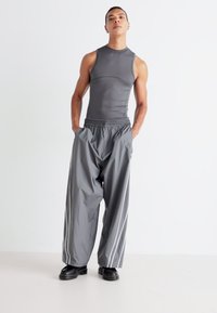 Gray sleeveless top with a fitted design paired with loose-fitting gray pants featuring white side stripes. Model wears black boots.