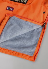 Veste orange avec côté partiellement dézippé, révélant une doublure en polaire grise douce, détail de la fermeture éclair et un patch avec le drapeau de la Norvège près du haut.