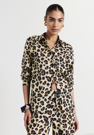 Camicia a motivo leopardato in beige e nero con maniche lunghe, bottone frontale e tasca sul lato sinistro. Texture liscia.