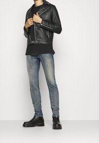 Svart läderbikerjacka med silverdragkedjor, lagd över en svart t-shirt. Bärs med blekta blå skinny jeans och svarta chelsea boots.