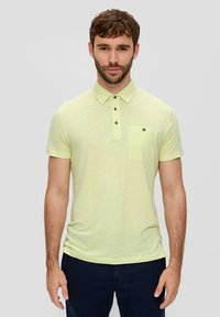 Koszulka polo z krótkim rękawem w jasnym żółtym kolorze, z kołnierzykiem, trzyguzikowym zapięciem i kieszonką na piersi z guzikowym detalem. Miękka tekstura.