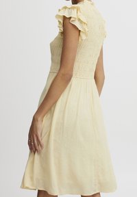 Gelbes Kleid mit kurzen Rüschensäumen, gerafftem Oberteil, strukturiertem Stoff und einem knielangen Rock mit kleinen erhabenen Punkten.