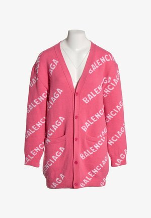 Cardigan rose vif avec boutons sur le devant, deux poches, et motif de texte blanc répété "BALENCIAGA" sur tout le tissu.
