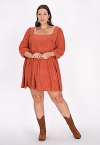 Rostfarbenes, wildlederähnliches Kleid mit quadratischem Ausschnitt, Puffärmeln und ausgestelltem Rock. Tragen mit braunen, spitzen Ankle Boots.