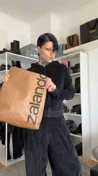 En brun Zalando-handlesekk med fet svart skrift. Personen har på seg en svart velour zip-up hettegenser og matchende bukser.