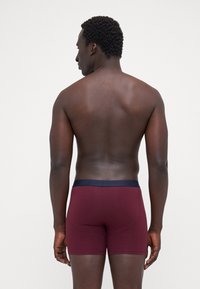 Männer Boxershorts in Maroon mit einem navyfarbenen elastischen Bund, mit einer glatten Textur und enganliegendem Design, von hinten gezeigt.
