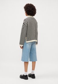 Maglione bianco e nero a scacchi houndstooth con colletto a costine, abbinato a pantaloni corti di jeans blu chiaro. Il modello indossa scarpe nere e calze bianche.