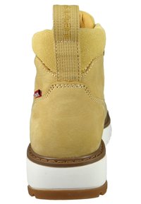 Beżowe zamszowe botki za kostkę z wyściełanym kołnierzem, kontrastującą białą podeszwą i teksturowanym uchwytem z tyłu. Zawiera akcenty w formie przeszyć.
