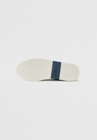 Semelle de chaussure en caoutchouc blanc avec un motif de grip texturé et une bande d'accent bleue portant le logo "REPLAY". Surface lisse, forme arrondie.