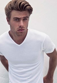 Witte korte mouwen v-hals t-shirt op een persoon met lichte huid en rommelig blond haar, geposeerd tegen een neutrale achtergrond.