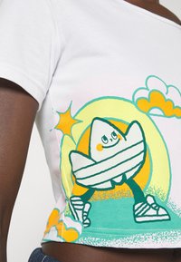 Vit bomullströja med en tecknad design av en glad karaktär omgiven av gula och gröna element, med korta ärmar och rundad krage.