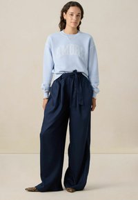 Lichtblauwe sweatshirt met "AMORE" in het wit, gecombineerd met losse, marineblauwe broeken met een gestrikt tailleband. Textuurstof en een ontspannen pasvorm.