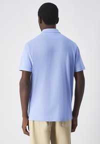 Jasnoniebieska koszula polo z krótkim rękawem i kołnierzykiem, o gładkiej fakturze i prostym wykończeniu dołu, noszona z beżowymi spodniami.