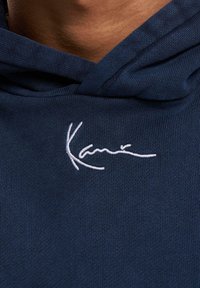 Sudadera azul marino con una textura suave y un ajuste holgado, con un detalle de firma bordado en blanco en la zona del pecho.