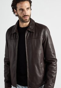 Braune Lederjacke mit Reißverschluss vorne, klassischen Kragen und zwei seitlichen Taschen. Das Material hat eine glatte Textur und einen dezenten Glanz.