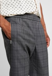 Grå rutiga byxor med en texturerad tyg, som har en zip-försedd sidficka och resårmidja för komfort.