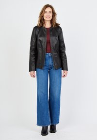 Mustat nahkatakki, jossa pyöreä kaula-aukko ja vetoketju, yhdistettynä korkeavyötäröisiin sinisiin leveälahkeisiin farkkuihin ja mustiin nilkkureihin.