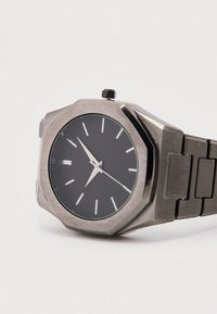 Achteckige silberne Metall-Uhr mit schwarzem Zifferblatt, silbernen Stunden- und Minutenzeigern sowie weißen Stundenmarkierungen auf einem Gliederarmband aus Metall.