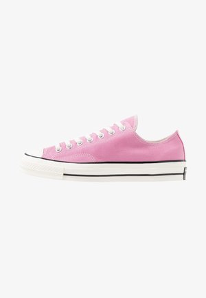 Zapatilla de lona rosa baja con cordones blancos, puntera de goma blanca y suela blanca con rayas negras.