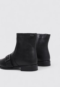 Bottines en cuir noir avec une texture lisse, présentant une fermeture éclair sur le côté, un détail de sangle et de boucle, et un talon bas en bloc.