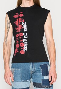 Czarny bezrękawnik z nadrukiem czerwonych ust i napisem "OUT OF MIND" białymi blokowymi literami. Materiał jest miękki i gładki.