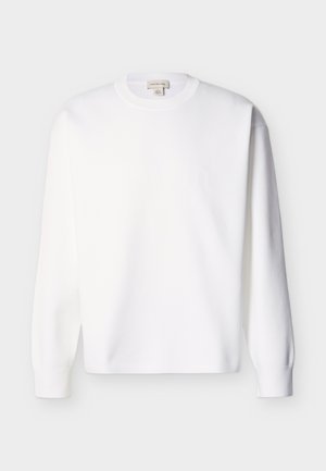 Hvit bomull genser med lang arm, rund hals og ribbestrikkede mansjetter. Enkel design uten synlige mønstre eller grafikk.