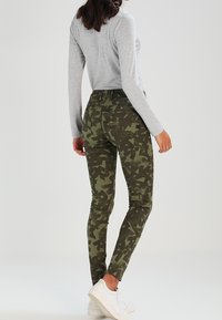 Olivgrön kamouflage-skinny jeans med olika geometriska mönster, hög midja och bakfickor, matchade med en ljusgrå långärmad topp.