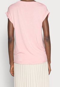 Camiseta de jersey rosa con mangas cortas enrolladas, textura suave y corte relajado, combinada con una falda ligera con plisados.