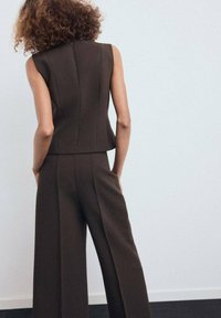 Top marrón sin mangas combinado con pantalones anchos marrones, con un diseño a medida y costuras sutiles. Tejido suave con un estilo minimalista.