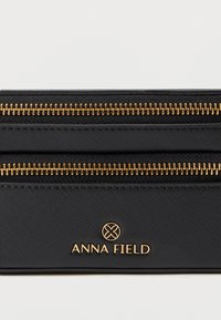 Μαύρο πορτοφόλι με χρυσά φερμουάρ και λογότυπο "ANNA FIELD". Διαθέτει υφή στο υλικό και δύο διαμερίσματα με φερμουάρ για ασφαλή αποθήκευση.