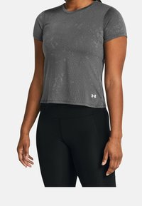 Šedé aktivní tričko s krátkým rukávem s texturovaným povrchem, které má kulatý výstřih a malé bílé logo na dolní levé straně.