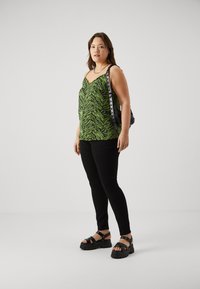 Green and black striped tank top, black skinny pants, chunky black sandals, metallic accents on bag, overall casual outfit design.