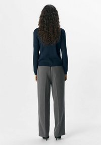 Pull fitted bleu marine associé à un pantalon gris à jambes larges, tissu texturé, finition lisse et design minimaliste, vu de dos.