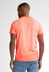 T-shirt a maniche corte in tessuto misto con una sfumatura di corallo brillante a rosa. Presenta un collo rotondo e una vestibilità rilassata vista da dietro.