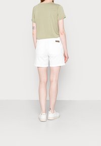 Haut à manches courtes vert olive associé à des shorts en coton blancs. Détails de logo visibles sur les shorts et baskets blanches avec semelles texturées.