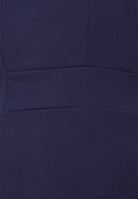 Tecido azul marinho com uma textura suave, apresentando costuras e detalhes de painéis. O material parece ser estruturado e bem ajustado.