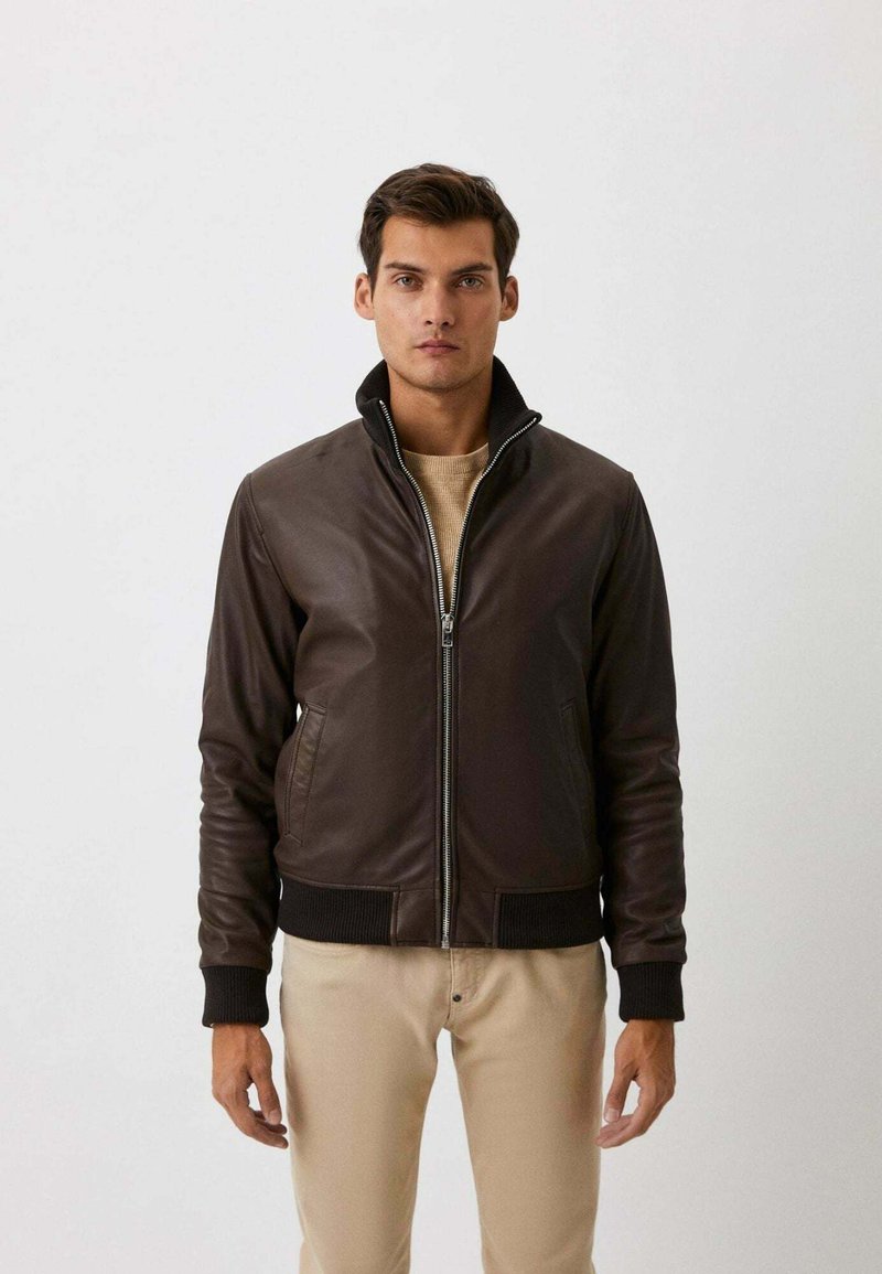 Bruine leren jas met een ritssluiting, geribbelde manchetten en kraag, met een gladde textuur en een slim fit ontwerp. Draagt over een beige top.