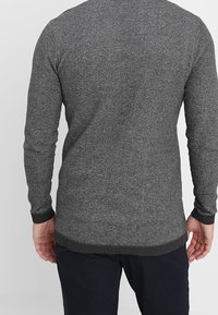 Gråstickad tröja med ett texturerat mönster, långa ärmar och ribbade muddar och nederkant. Har en rundad halsringning och en lätt avsmalnande passform.