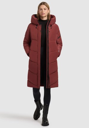 Doudoune bourgogne avec une grande capuche, fermeture éclair, motif en chevron et poches avant, portée sur des leggings noirs et des bottines.