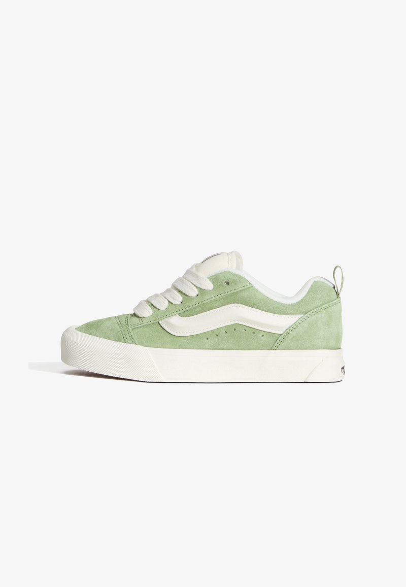 Baskets basses avec tige en daim vert clair, bande blanche en forme de vague, semelle blanche épaisse et lacets blancs, montrées de profil.