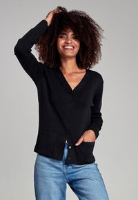 Sort cardigan med V-hals, lange ærmer, knaplukning foran og to lommer; parret med lyseblå jeans.