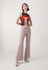 Top court noir avec un motif graphique rouge, associé à un pantalon taille haute évasé à rayures rouges, bleues et blanches. Talons transparents.