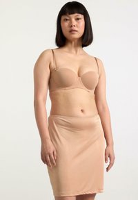 Beige bh med glatte, polstrede skåle og justerbare stropper, parret med en matchende beige blyantskirt, begge lavet af strækbart stof.
