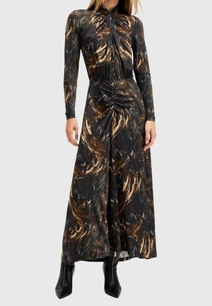 Femme portant une robe longue noire à manches longues avec des motifs abstraits brun et or ressemblant à des plumes, associée à des bottines noires zippées.