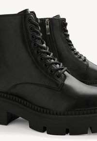 Bottines noires en cuir à lacets avec fermeture éclair latérale et semelles épaisses à crampons, vues en gros plan sous un angle latéral.