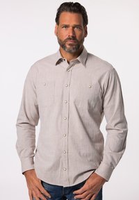 Camicia a maniche lunghe beige chiaro in un tessuto strutturato. Presenta due tasche sul petto e bottoni chiari. Indossata con jeans blu.