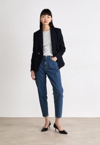 Marineblauwe dubbelbreasted blazer met gouden knopen, grijze crewneck t-shirt, high-waisted blauwe spijkerbroek en zwarte puntige hakken.
