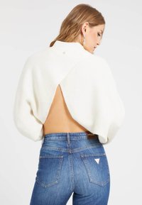 Pull en maille blanche avec un décolleté dans le dos, assorti à un jean bleu avec un label de marque et des accents de poches. Texture douce, coupe ample.